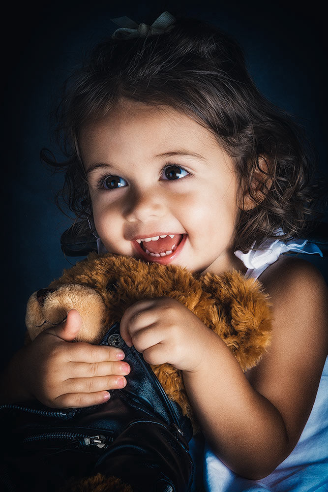 Portrait of a little girl holding her teddy bear while showing her fangs