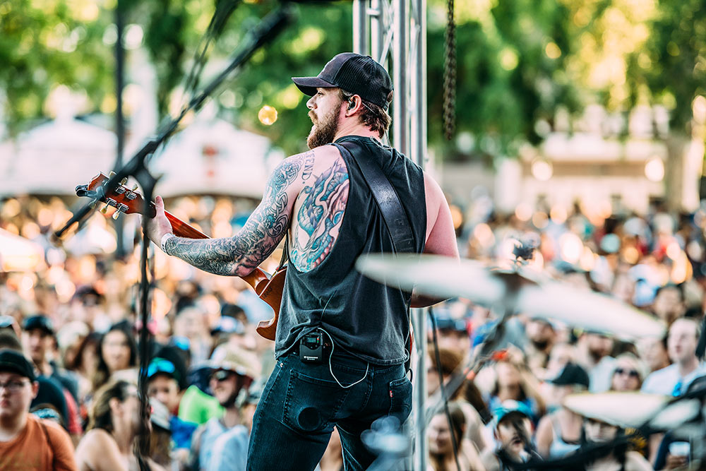 A guitarist in black displaying his tattoos playing a concert