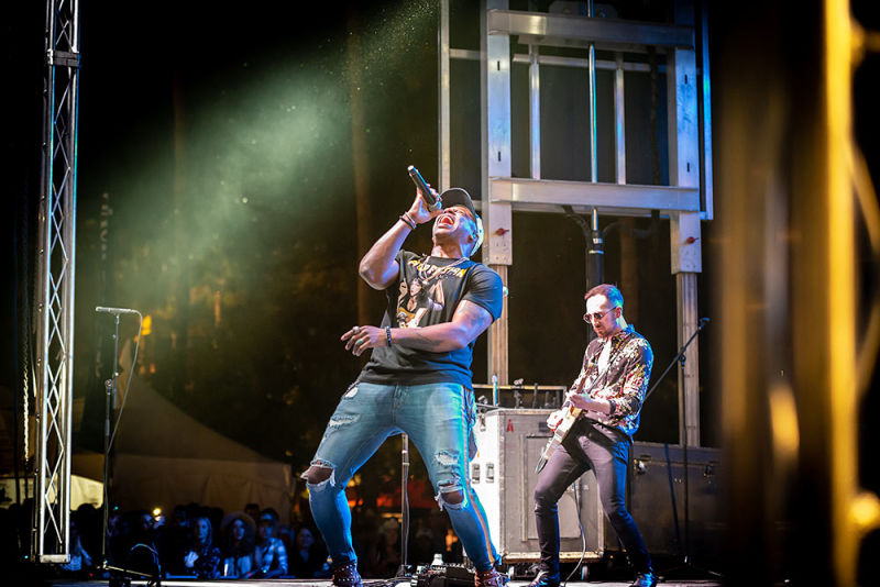 A male lead singer of a band rocks the house while a guitarist is visible behind him on stage