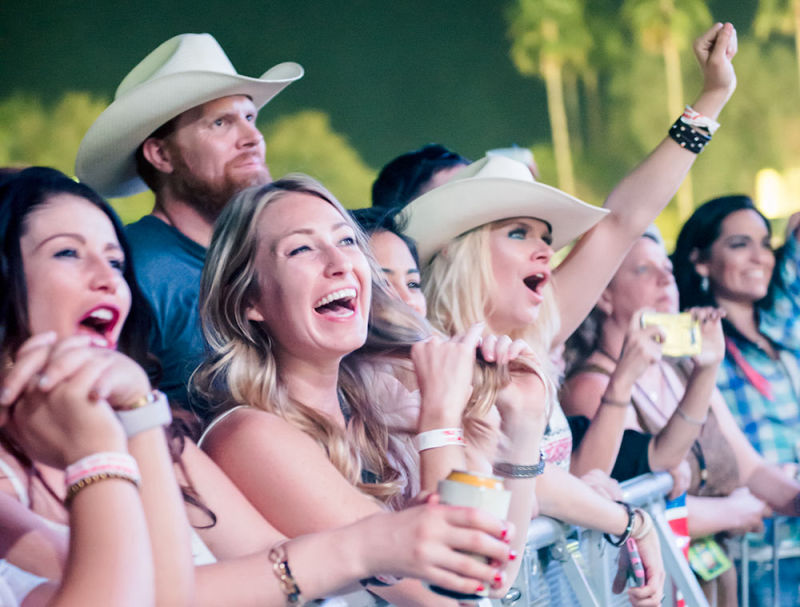 Excited girls in the front row cheerfully smiling and waving to the band