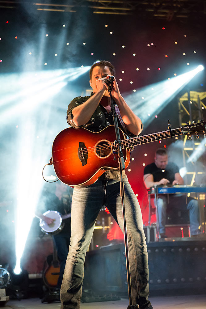 Easton Corbin singing in front of stylish lights and fog with a glowing acoustic guitar