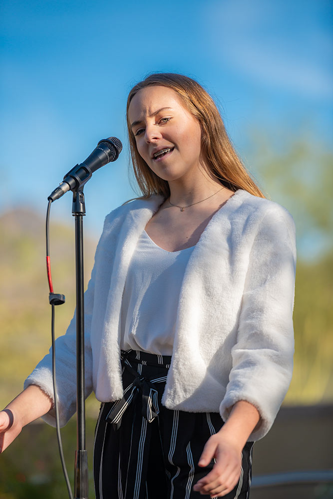 Young lady performer in a white fur coat sings in front of an audience