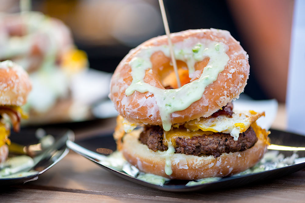 Hamburger samples with donut buns dripping with sauce at an event