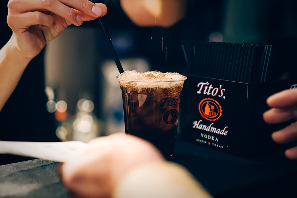 Bartender mixing a drink at a bar top next to a Tito's branded holder