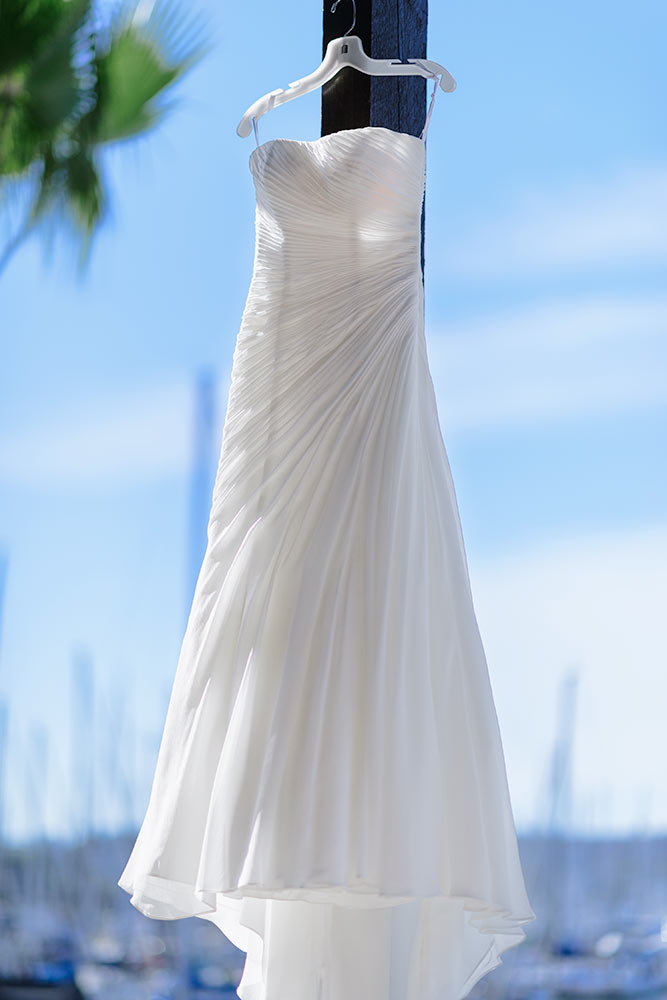 Wedding dress on a hanger blowing in the wind with sail boats in the pier in the background