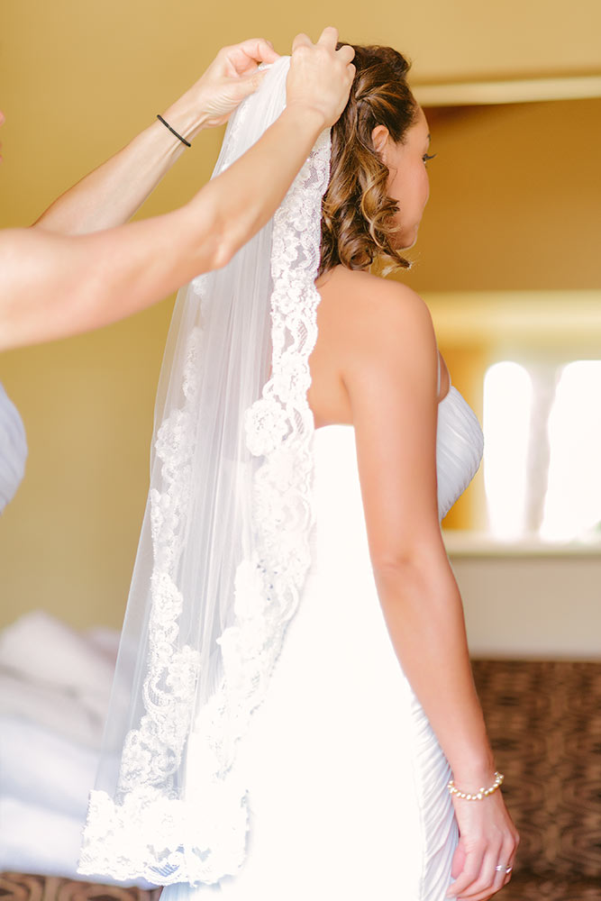 Dressing a happy bride with the veil in a yellow brightly lit room 