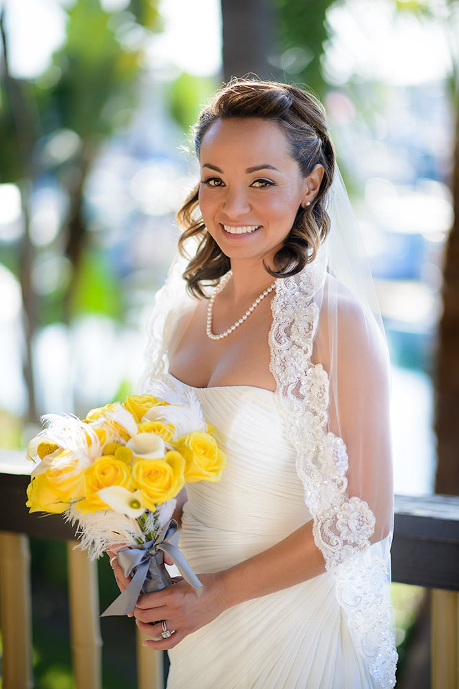Happy bride wearing all white with yellow and white flowers in front of a pier