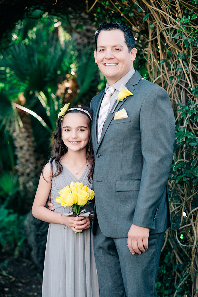 Groom wearing all gray hugging daughter who is holding yellow flowers