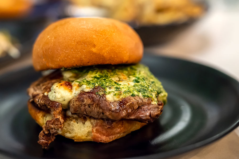 Interesting burger offering with melted sauce sitting on a black plate