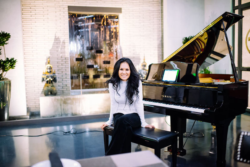 Woman posing on a piano bench in front of a grand piano