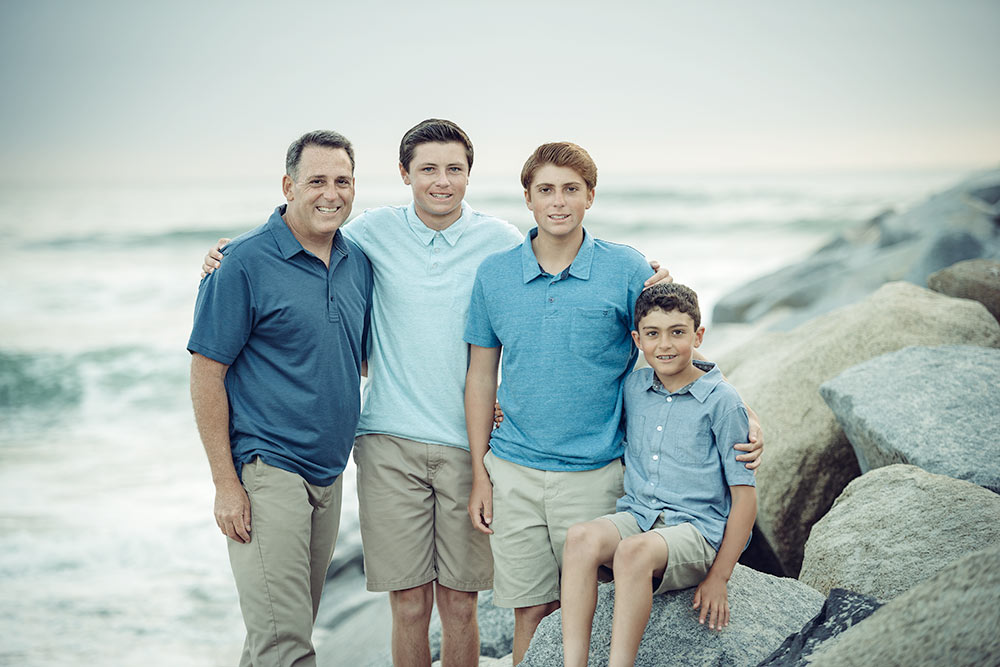 Dad with his 3 sons hugging on the beach during a wintery day