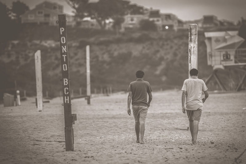 Sepia old-style photo of a telephoto scene of a beach with 2 boys walking with backs to the camera