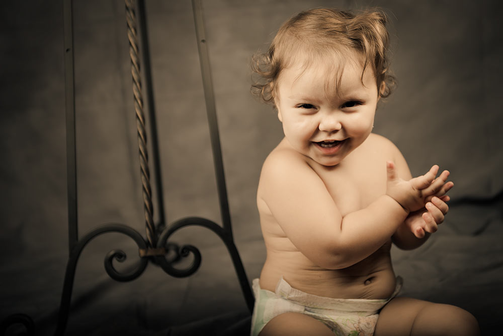 Little baby girl in diapers posing in a studio while laughing