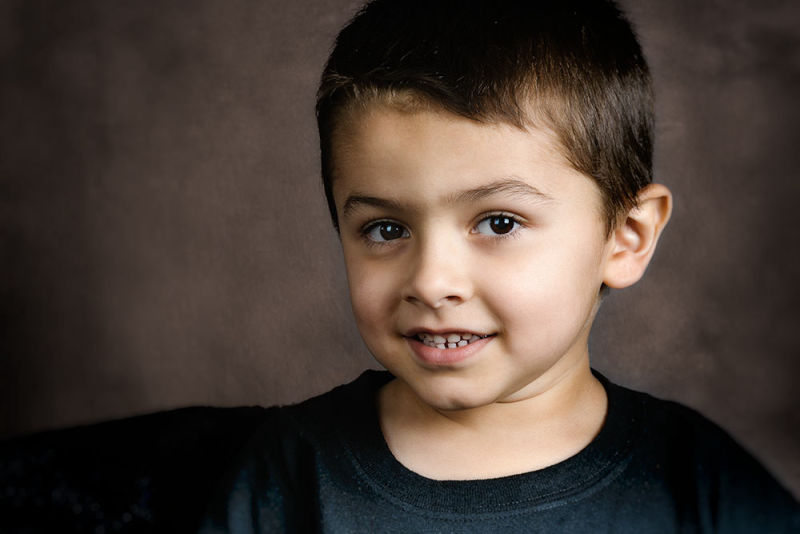 Young boy smiling in a studio portrait with a brown background