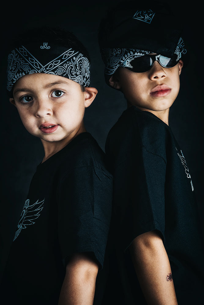 Two young boys posing as gangsters set in a moody dark room lit with studio lights