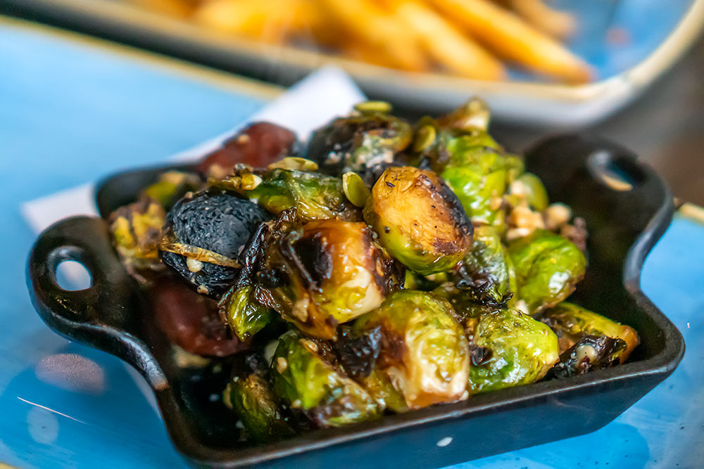 Brussel sprouts in a hot skillet with french fries in the background