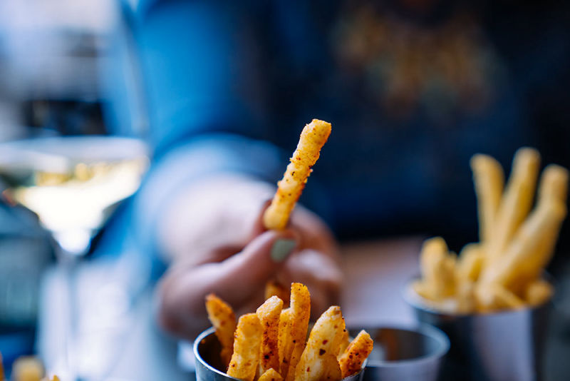 French fries with seasoning on a table with wine and someone with a blue shirt