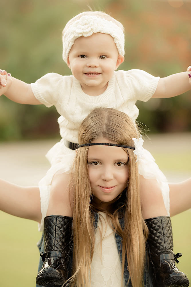 Young girl holding a little baby on her shoulders and dancing in the sun at a park