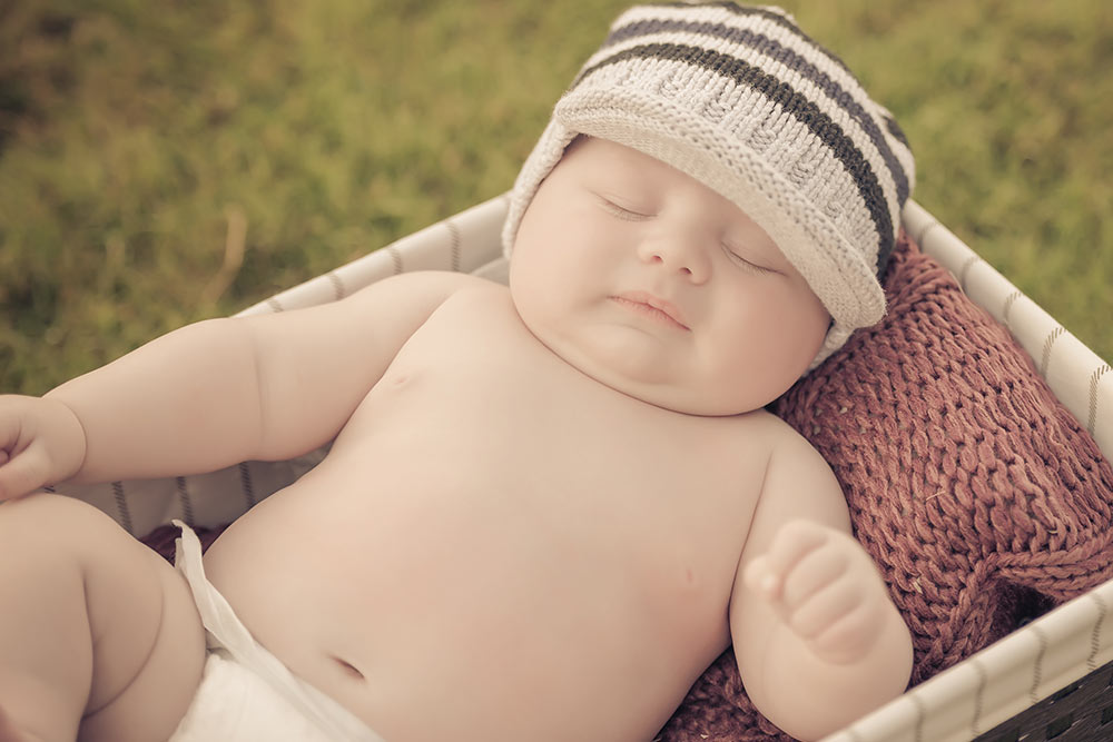 little baby boy only dressed in a diaper laying in a bassinet on the grass