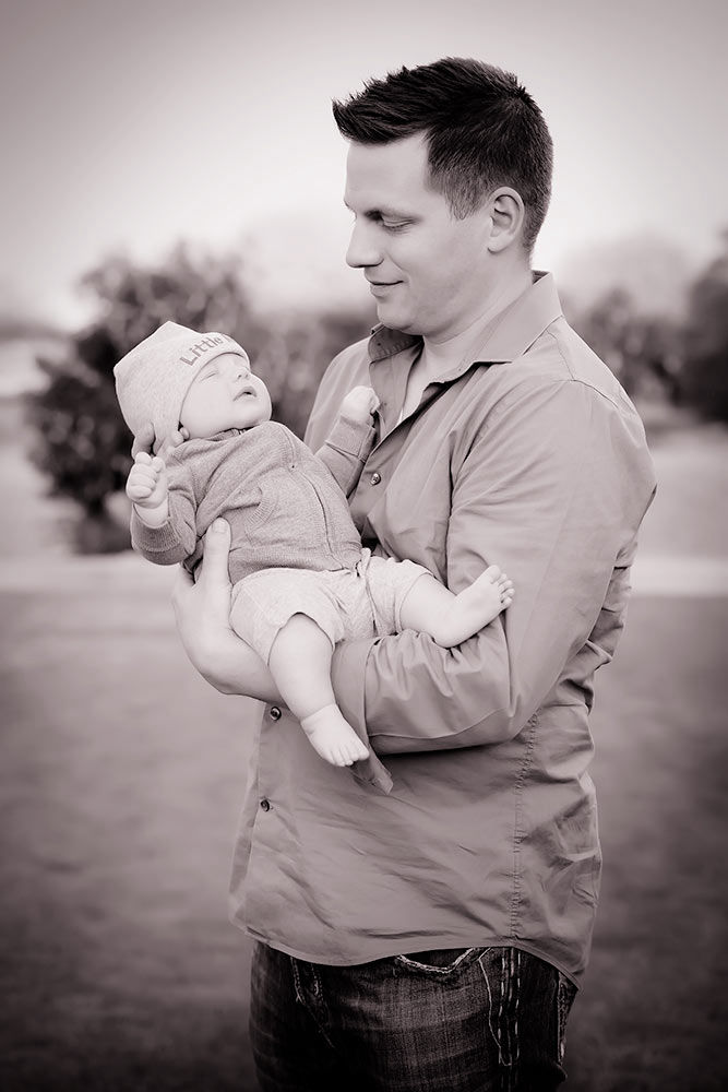 Black and white proud father holding his baby boy and smiling down upon him