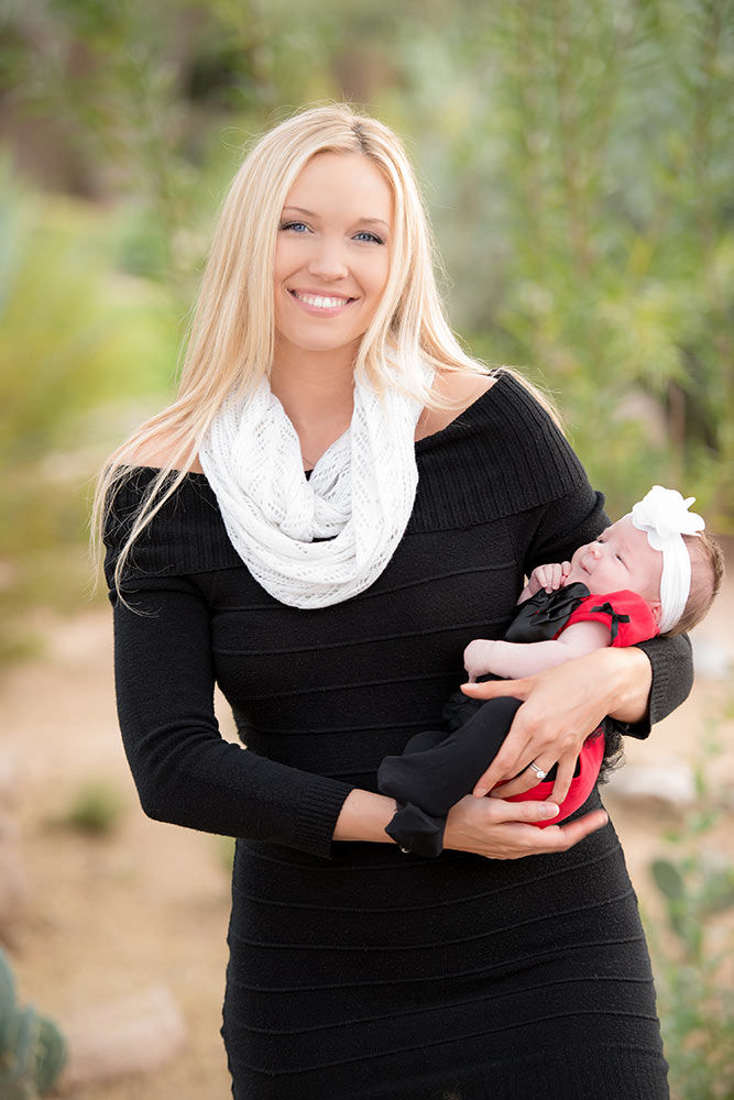 Mother in black dress and white scarf holding her little baby in her arms at the park