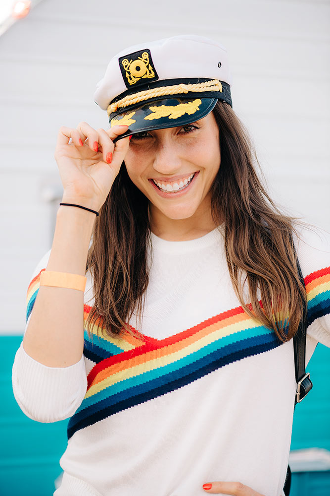 Rainbow shirt on a model who is posing with a captains hat tilting it while playfully smiling