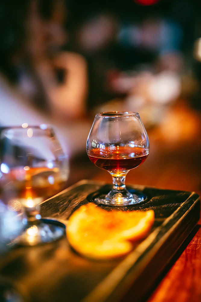 A whiskey flight with orange and liquors on a wooden flight board