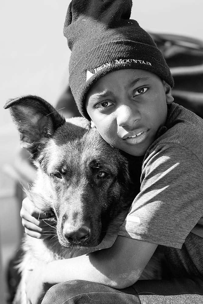 Portrait of a little boy wearing a black beanie holding his german shepherd dog