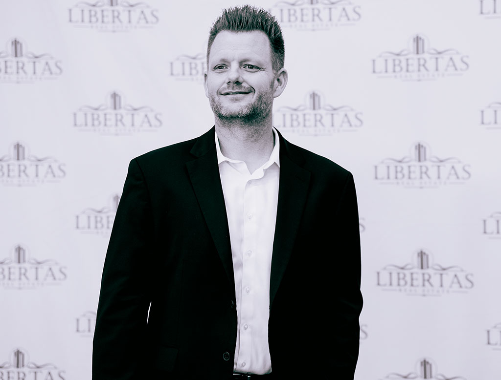 Founder Justin Thorstad of Libertas captured in black and white, standing confidently in front of a logo-adorned wall