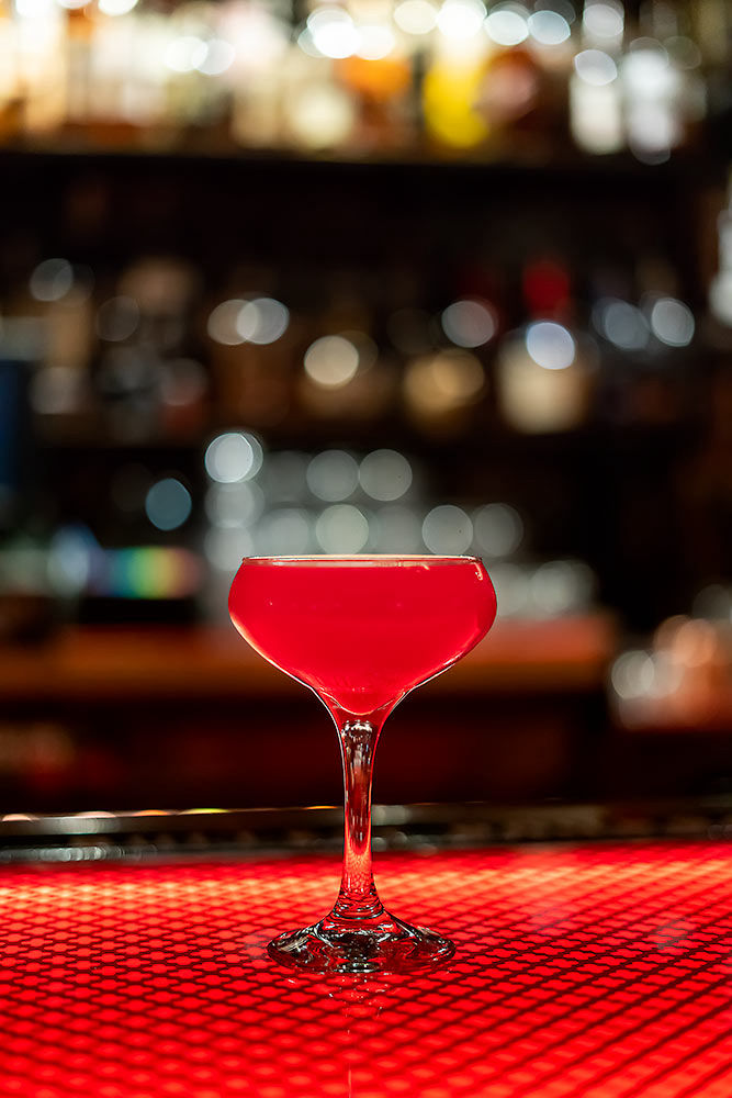 Red cocktail drink at a lit up bar with spirits in the background