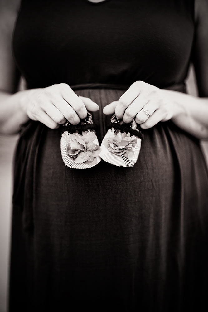 Proud momma to be in black dress carefully displays her baby's little shoes