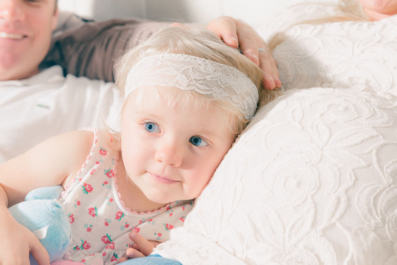 Little baby girl happily rests her head against her momma's pregnant belly