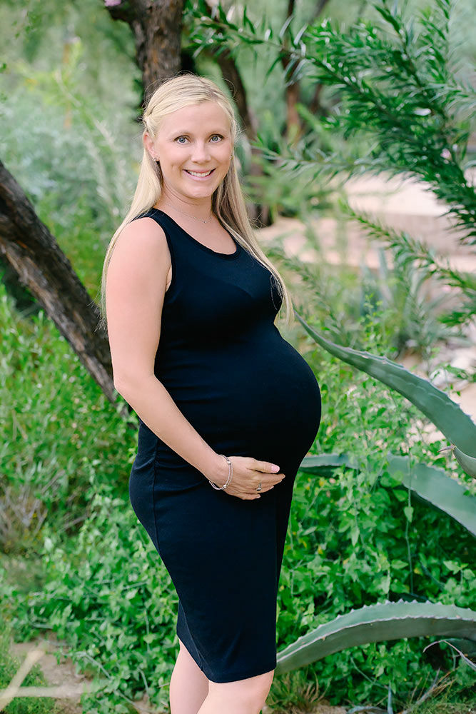 Stylish pregnant woman in a black dress, surrounded by natural beauty