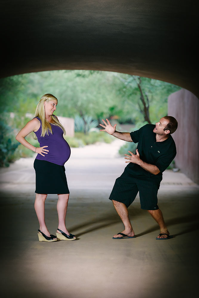 Pregnant couple sharing a lighthearted moment under a bridge