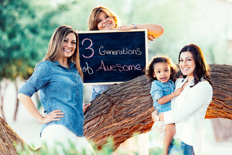 3 generations displayed on a chalk board while the family of ladies smile next to a large tree trunk